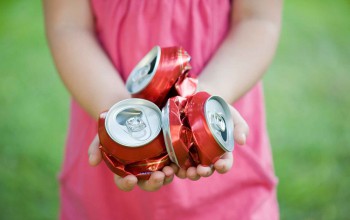 a girl holding three crushed cans