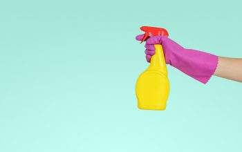 A spray bottle being sprayed by a hand in a pink rubber glove