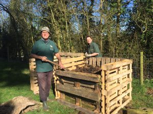 Two people standing next to a homemade wooden compost bin