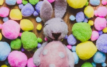 Picture of felted craft Easter bunny, laying down, holding a felted egg and surrounded by colourful felted mini egg shaped balls.