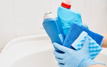 Rubber gloved hands holding a range of cleaning supplies above a bathroom sink