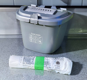 A 7 litre food waste kitchen caddy sat on a kitchen worktop next to a roll of caddy liner bags.
