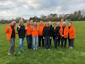 A group of 13 Environment Action Volunteers stood together in a green space wearing matching black and orange uniforms